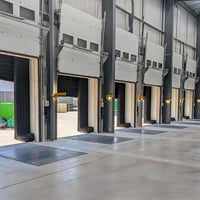 Multiple industrial garage doors in a warehouse setting with yellow swing arm dock lights mounted between each.