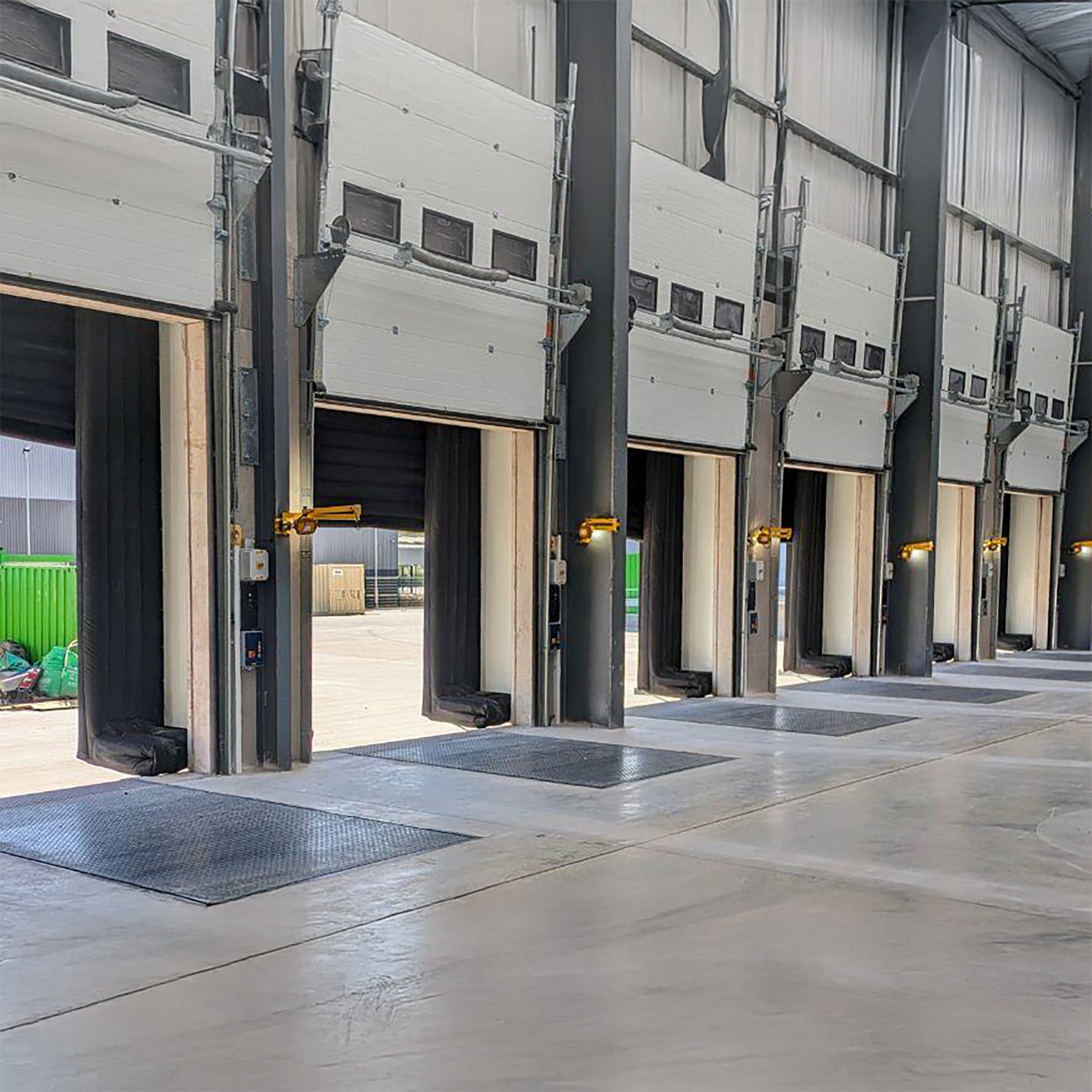 Multiple industrial garage doors in a warehouse setting with yellow swing arm dock lights mounted between each.