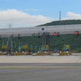 Highway toll booth with LED traffic lights and barriers under a clear blue sky.