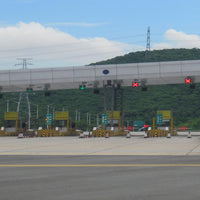 Highway toll booth with LED traffic lights and barriers under a clear blue sky.